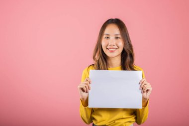 Asyalı mutlu bir genç kız portresi. Elinde beyaz bir A4 reklam stüdyosu posteri var. Pembe arka planda izole edilmiş bir fotoğraf.