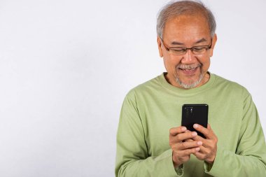 Beyaz arka planda izole edilmiş bir cep telefonu stüdyosu fotoğrafı tutan gülümseyen Asyalı yaşlı bir adam. Elinde cep telefonuyla mesaj yazan yaşlılar. Bağlantı ve iletişim kavramı