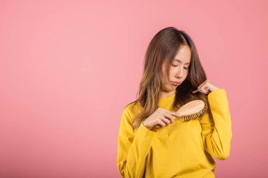 Genç ve güzel Asyalı bir kadın tarağı ve sorunlu saçı yüzünden üzgün, portre kadın saç dökülmesi sorunu yaşıyor, stüdyo çekimi pembe arka planda, ilaç sağlık konsepti