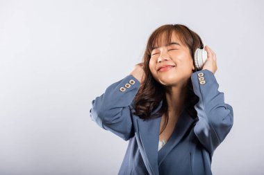 Mutlu Asyalı genç bayan gülümsüyor, telefonunda Bluetooth kulaklıkla müzik dinliyor. Beyaz arka planda stüdyo çekimi. Modern teknolojiye dalmış ve zamanının tadını çıkarıyor..