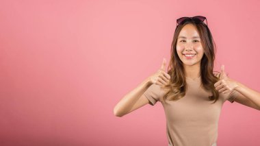 Asyalı güzel, gülümseyen genç bir kadın parmağını kaldırdı. Tamam, kabul et. Stüdyo çekimi pembe arka planda, Taylandlı bir kadın, fotokopi alanındaki parmak hareketi kadar başarılı.