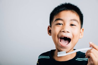 Üst süt dişini kaybeden sevimli bir Asyalı çocuk diş fırçası tutuyor diş bakımını ve öğrenmenin mutluluğunu gösteriyor. Beyaz arka planda izole edilmiş. Çocuk dişçi rutini