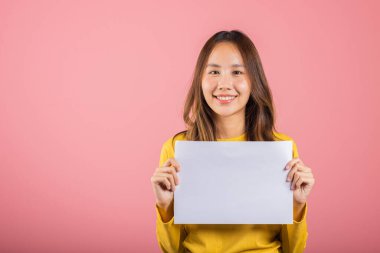 Asyalı mutlu bir genç kız portresi. Elinde beyaz bir A4 reklam stüdyosu posteri var. Pembe arka planda izole edilmiş bir fotoğraf.