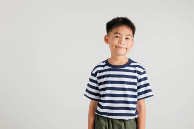 Asyalı sevimli çocuk gülümsüyor ve mutlu bir şekilde stüdyoda duruyor beyaz arka planda izole edilmiş, ilkokul çocuğu portresi, Taylandlı çocuk.