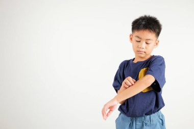 Asyalı küçük çocuk, beyaz arka planda izole edilmiş bir fotoğraf stüdyosundaki sivrisinek ısırığından kaşınan koluyla kaşınan Tayland ilköğretim dermatiti ve uyuz, alerji belirtileri, sıtma günü konsepti.