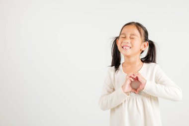 Gülümseyen Asyalı genç bir kız güven gösteriyor. Beyaz arka planda elleri ve parmakları olan bir kalp şekli yaratıyor. Anaokulu çocuğunun portresi Sevgililer Günü 'ne sevgilerini gönderiyor.