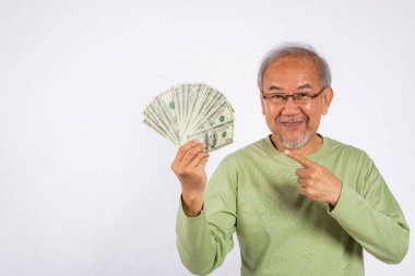 Asyalı gülümseyen yaşlı adamın portresi elinde bir tomar para ve beyaz arka planda izole edilmiş stüdyo çekimini işaret ediyor. Mutlu kıdemli adam parayı işaret ediyor nakit para banknotları hayranı
