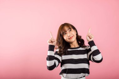 Asyalı mutlu bir portre ayakta duran güzel bir genç kadın jest yapıyor. İki parmak yukarıda bir şey sunuyor. Stüdyo çekimleri pembe arka planda, fotokopi alanı ile izole edilmiş.