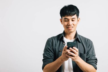 Hevesli bir Asyalı ergen internet iletişimi için akıllı cep telefonuna mesaj yazarken gülümsüyor. Stüdyo çekimi beyaz arka planda izole edilmiş, teknolojiden zevk aldığını vurguluyor.