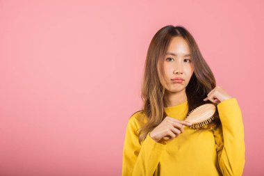 Genç ve güzel Asyalı bir kadın tarağı ve sorunlu saçı yüzünden üzgün, portre kadın saç dökülmesi sorunu yaşıyor, stüdyo çekimi pembe arka planda, ilaç sağlık konsepti