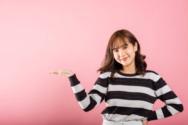 Asyalı mutlu bir portre güzel tatlı bir genç kadın gülümsüyor. Elinde bir şey tutan bir ürünü sunuyor. Stüdyo resmi pembe arka planda, fotokopi çekiliyor.