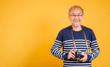 Asyalı, elinde klasik SLR kamera olan yaşlı bir adamın portresi izole edilmiş sarı arka plan, gülümseyen yaşlı fotoğrafçı gri saçlı eski moda kamera tutuyor.