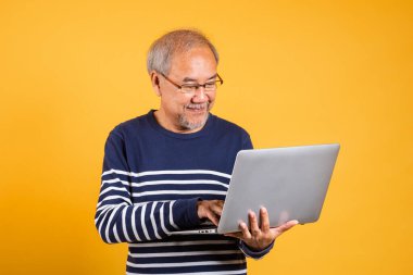Gözlüklü Asyalı yaşlı adam dizüstü bilgisayar stüdyosu kullanıyor izole edilmiş sarı arka plan, gülümseyen yaşlı adam beyaz saçlı, insanların yaşam tarzı.