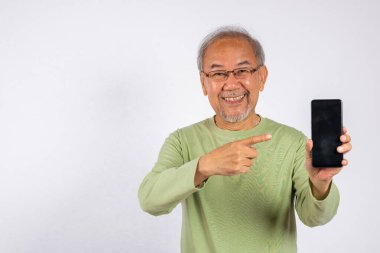 Cep telefonu tutan Asyalı gülümseyen yaşlı adamın portresi ve beyaz arka planda izole edilmiş boş ekran stüdyo çekimini gösteren cep telefonu ekranı gösteren mutlu yaşlı adam.