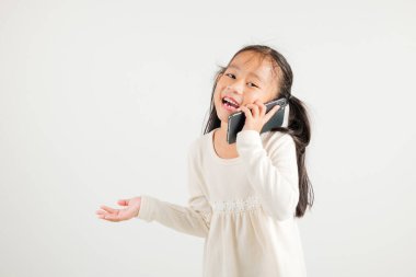 Mutlu Asyalı genç kız gülümsemesi heyecanlı konuşan akıllı cep telefonu stüdyosu beyaz arka planda izole edilmiş Tayland anaokulu çocuğu akıllı telefondan jest yapıyor.