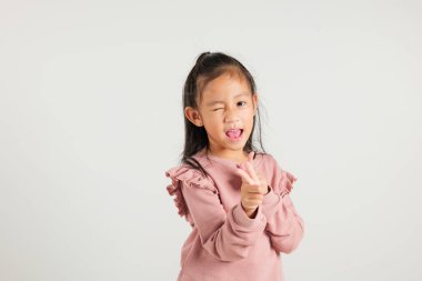 Neşeli Asyalı genç kız kameraya iki silah parmağı hareketi yapıyor. Dost canlısı ve küstah bir ifadeyle. Beyaz arka plana izole edilmiş, anaokulu çocuğu pozitif ve neşe yayıyor.