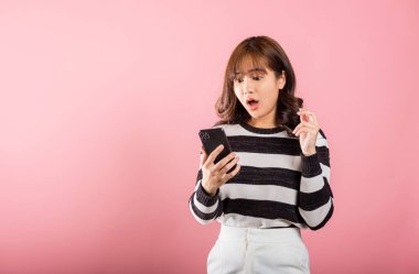 Telefondan korkan, telefonda kötü haber görmekten korkan, cep telefonuyla şok olan, pembe arka planda izole edilmiş stüdyo çekimleriyle şaşırmış genç, güzel Asyalı kadın.