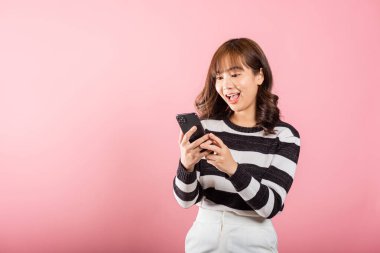 Mutlu Asyalı portre güzel güzel genç kız cep telefonu kullanarak heyecanla gülümsüyor evet de, pembe arka planda izole edilmiş stüdyo çekimi, Taylandlı kadın şaşırdı akıllı telefondan kazanan jest yaptı