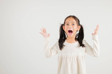 Sevinçli bir kız çocuğu başarısını kutlamak için heyecanla evet diyerek yumruklarını kaldırıyor. Beyaz arka planda çekilen mutlu bir anaokulu çocuğunun Asyalı portresi.