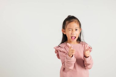 Neşeli Asyalı genç kız kameraya iki silah parmağı hareketi yapıyor. Dost canlısı ve küstah bir ifadeyle. Beyaz arka plana izole edilmiş, anaokulu çocuğu pozitif ve neşe yayıyor.