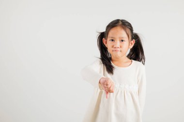 Morali bozuk Asyalı genç bir kızın portresi, hoşnutsuzluğu sembolize eden bir jest sergiliyor. Stüdyo görüntüsü beyaz, fotokopi alanı var, anaokulu çocuğu negatif ve üzgün bir görünüm sergiliyor.