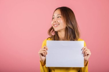 Asyalı mutlu bir genç kız portresi. Elinde beyaz bir A4 reklam stüdyosu posteri var. Pembe arka planda izole edilmiş bir fotoğraf.