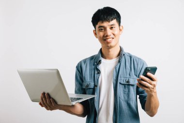 Portre Asyalı gülümseyen genç adam dizüstü bilgisayar ve cep telefonu stüdyosu izole edilmiş beyaz arka plan, Happy heyecanlı iş adamı bilgisayar ve akıllı telefon, modern teknoloji ve önem kullanıyor.