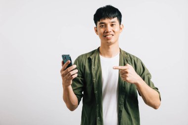 Gülümseyen genç bir Asyalı güvenli bir şekilde online alışveriş için akıllı telefon ekranını işaret ediyor. Stüdyo portresi, beyaz tenli, zarif teknoloji kullanımına izole edilmiş. Boşluğu kopyala.