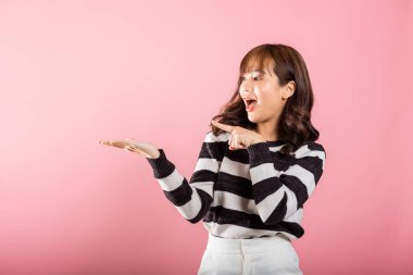 Asya 'nın mutlu portresi. Güzel bir kadın avucunun içinde bir şeyi tutuyor ve parmağıyla ona bakıyor. Stüdyo resmi, pembe arka planda, fotokopi alanı ile izole edilmiş.