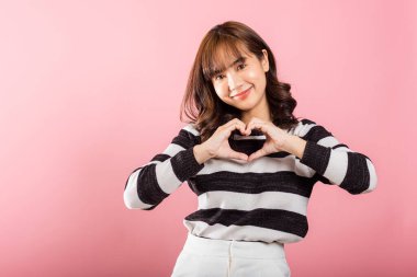 Gülümseyen Asyalı bir kadın, pembe arka planda elleri ve parmaklarıyla kalp şekli oluşturarak kendine güvenini gösterir. Sevgililer Günü 'ne sevgilerini gönderen güzel bir genç bayanın portresi..