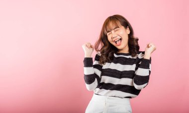 Başarılı bir Asyalı kadın portresi. Neşeli bir profilde. Yumruklarını gülümseyerek kaldırıyor. Stüdyo çekimi pembe, zafer ve heyecanı ifade ediyor..