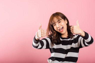 Pembe arka planda, stüdyo portresindeki kendine güvenen Asyalı bir kadın onay işareti yapıyor. Anlaşmayı ve başarıyı simgeliyor. Neşeli gülümsemesi pozitiflik ve memnuniyet saçıyor..