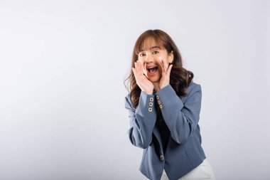 Bu stüdyo çekiminde, genç bir Asyalı kadın eli ağzında duruyor ve heyecanlı haberleri sessiz bir tonda paylaşıyor. Beyaz arkaplanda izole edilmiş, mesaj veya metin için boşluk bırakılıyor.