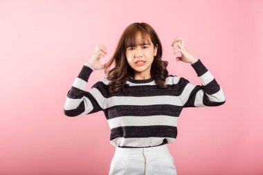 Asyalı mutlu bir portre güzel genç bir kadın kızgın ve kızgın duruyor sinirli ve öfkeli bir şekilde yumruğunu kaldırıyor öfkeyle inzivaya çekilmiş bir şekilde bağırıyor pembe arka planda stüdyo çekimi ve kopyalama alanı.