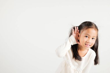 Asyalı genç bir çocuğun portresi, kulak misafiri olurken gülümsemesi kulak misafiri oluyor. Kulak üstüne kulak çekimleri, beyaz arka planda izole edilmiş fotokopi odası işitme hareketi, anaokulu kızı.