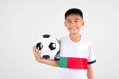 Genç bir çocuk bir futbol topu tutuyor ve gülümsüyor. Çocuk üzerinde 7 yazan beyaz bir gömlek giyiyor.