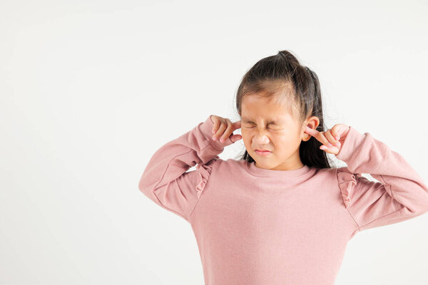Asian young kid girl expression of pain and frustration is evident as she covers ears and closes eyes with fingers to escape the loud noise in studio shot isolated white background, kindergarten child