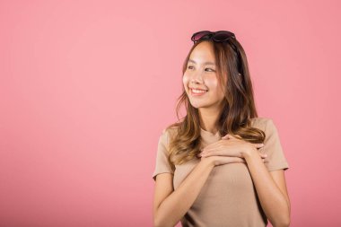 Güzel Asyalı genç kadın stüdyo çekimlerinde teşekkür ettiği için göğsüne dokunuyor. Pembe arka planda izole edilmiş, mutlu, büyüleyici bir kadın gülümseyen, göğsüne yakın, minnet dolu bir jestle el ele tutuşuyor.