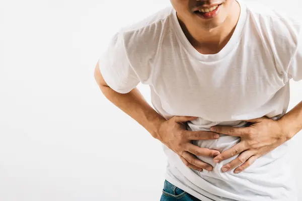 stock image An Asian man in distress due to stomachache and abdominal pain, reflecting digestive issues. Studio shot isolated on white background, symbolizing health and medical concerns.