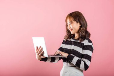 Mutlu Asyalı güzel bir kadının portresi dizüstü bilgisayarla gülümseyen bir yüz tutuyor kameraya bakıyor, pembe arka planda izole edilmiş bir stüdyo fotoğrafı, fotokopi odası, dizüstü bilgisayar.