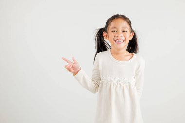 Mutlu Asya portresi gülümseyen küçük kız parmak boşluğunu gösteriyor, stüdyo resmi beyaz arka planda izole edilmiş, Tayland anaokulu çocuğu kopya alanı ile işaret ediyor.