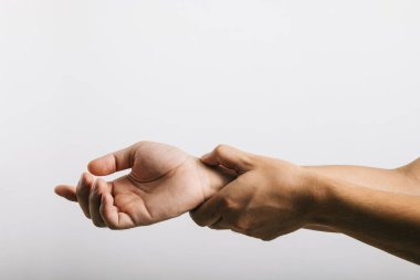 Rahatsız Asyalı bir gencin portresi bilek ağrısı gösteriyor. Karpal tünel sendromuyla bağlantılı olabilir. Stüdyo çekimi beyaz arka planda izole edilmiş, sağlık hizmetleri ve sağlık durumunun vurgulanması.