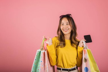 Asyalı mutlu bir genç kadın portresi. Gülümseyen bir genç kız. Elinde online alışveriş çantaları, cep telefonunda renkli ya da pembe arka planda izole edilmiş akıllı telefon stüdyoları var.