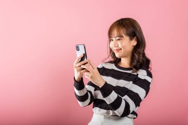 Mutlu Asyalı portre güzel güzel genç kız gülümseyen akıllı cep telefonu stüdyolarını kullanarak heyecanlı pembe arka planda izole edilmiş, Taylandlı kadın akıllı telefondan birinci sınıf jest yaparak şaşırttı.