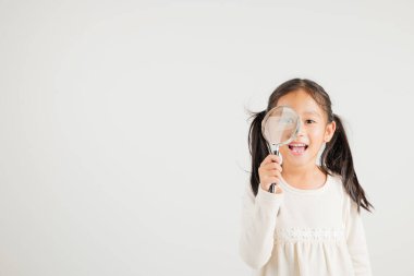 Beyaz arka planda izole edilmiş büyüteçten bakan Asyalı küçük bir kız çocuğu, mutlu bir anaokulu çocuk yaşam tarzı gülümsemesi büyüteç arayışı, eğitim.