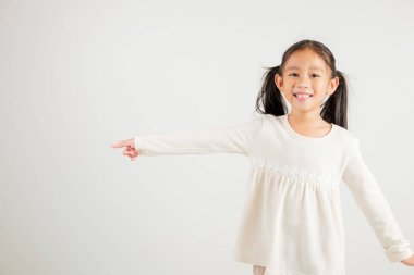 Mutlu Asya portresi gülümseyen küçük kız parmak boşluğunu gösteriyor, stüdyo resmi beyaz arka planda izole edilmiş, Tayland anaokulu çocuğu kopya alanı ile işaret ediyor.