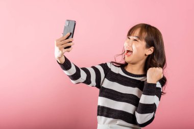 Mutlu bir Asyalı portresi güzel bir genç kız cep telefonu kullanarak heyecanla gülümsüyor. Evet deyin. Stüdyo çekimi pembe arka planda, Taylandlı kadın şaşırdı.