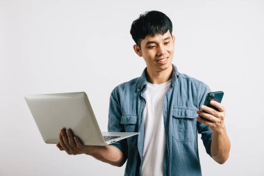 Portre Asyalı gülümseyen genç adam dizüstü bilgisayar ve cep telefonu stüdyosu izole edilmiş beyaz arka plan, Happy heyecanlı iş adamı bilgisayar ve akıllı telefon, modern teknoloji ve önem kullanıyor.