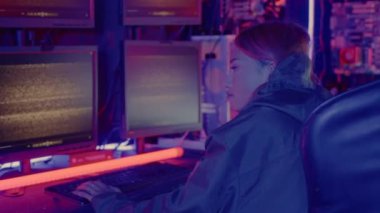 Siyah ceketli Asyalı bir kadın bilgisayar programlama sistemini hackliyor ve karanlık ofiste bilgisayar monitörüyle çalışıyor. Siber güvenlik sitesi geliştirme, siber güvenlik, bilgi izleme...