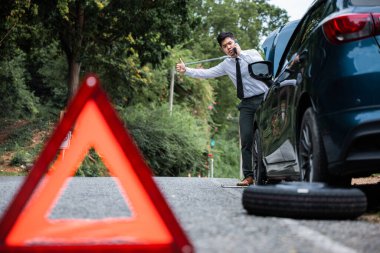 Uyarı üçgeniyle yolda duran bir adam azarlanan bir telefon alıyor. Asyalı iş adamı yardım istiyor ve baş parmağını kaldırıyor. Trafik ve iletişim sorunları kavramı.